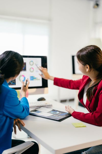 Two businesswomen discussing financial data on a computer, strategizing for the future with teamwork and collaboration Two businesswomen discussing financial data on a computer, strategizing for the future with teamwork and collaboration